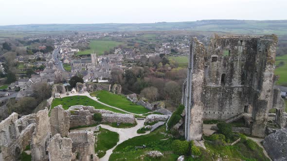 Aerial drone flview over Corfe Castle ruins perched on hill and green English countryside, UK