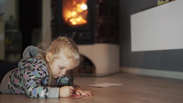 Little Girl Lying on the Floor in the Room Writing and Drawing. 
