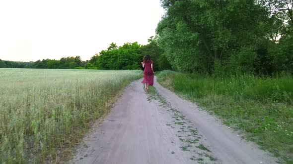 Young Woman with Long Hair in Long Dress Runs on a Field Road, Slow Motion  Shot