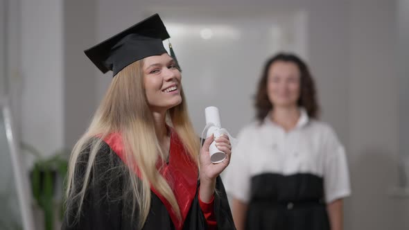 Happy Excited Graduate Posing with Rolled Diploma Looking Back at Blurred Woman