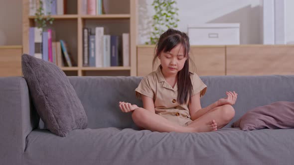 An Asian girl make meditation on the grey couch in the living room