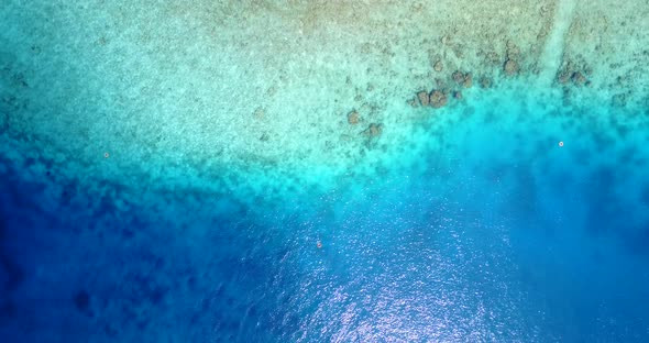 Daytime flying clean view of a sandy white paradise beach and aqua blue water background