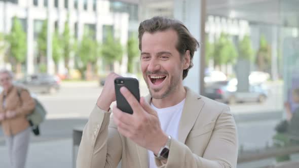 Young Man Celebrating Online Success on Smartphone Outdoor