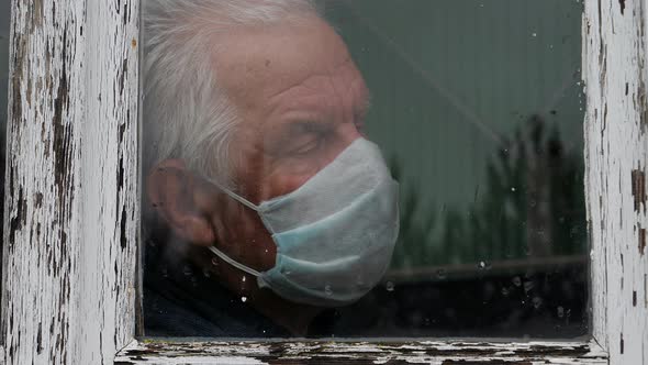 At Pandemic Covid Old Man In Medical Mask Looks Sadness Out Of Window At Street