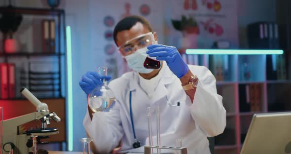 Male Chemist in Protective Mask and white Coat Conducting Chemical Experiment with Fluids