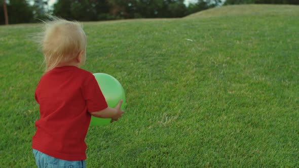 Adorable Toddler Going on Green Field Barefoot. Boy Holding Ball in Hands
