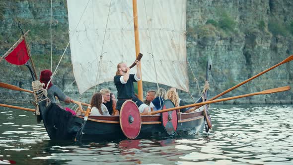 Vikings Sail on an Old Ship with a Raised Sail on a Calm River