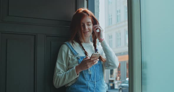 Young woman leaning against a door while using a smartphone