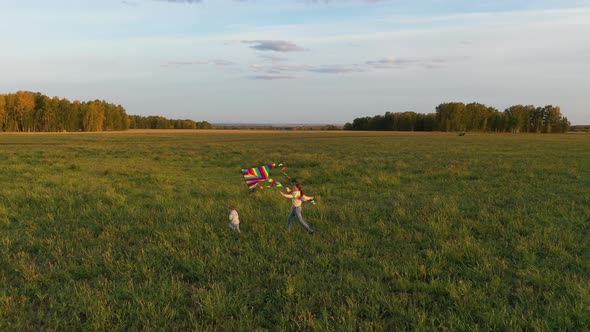 The Mother and Boy Run with a Kite on a Green Field