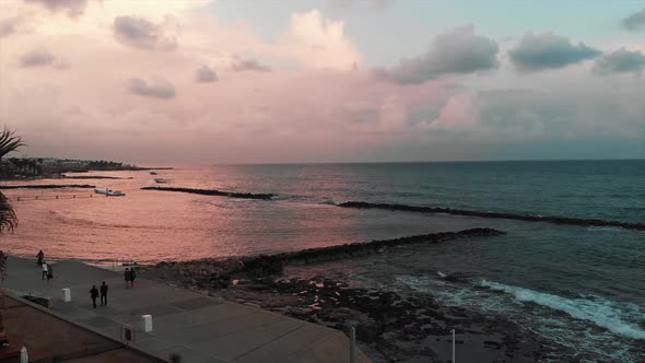 Tourists walking along promenade and enjoying vacation near calm sea at the sunset in Paphos Cyprus