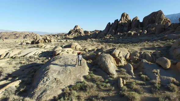 Aerial shot of a young man backpacker standing on a boulder with his dog in a desert mountain range.