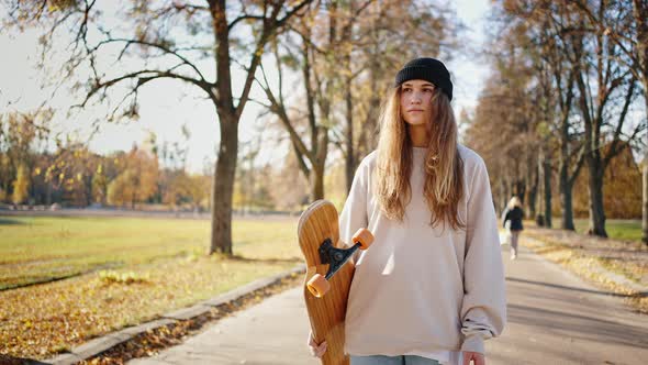 Sunny Close Portrait of a Young Teenage Girl in an Autumn Park with a Skateboard in Her Hands