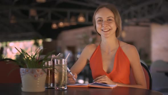 Woman Turns Diary Pages Smiles at Table with Juice