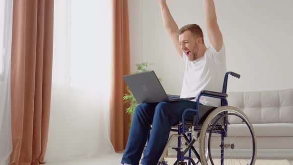 Cheerful Happy Disabled Person Rejoices at Good News While Sitting in Wheelchair with Laptop