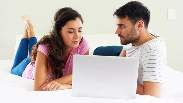 Couple interacting with each other while using laptop on bed