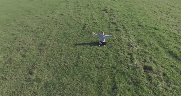 Low Orbital Flight Around Man on Green Grass with Notebook Pad at Yellow Rural Field.