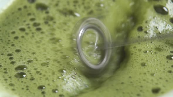 Whipping frothing green matcha tea with an electric spiral metal frother