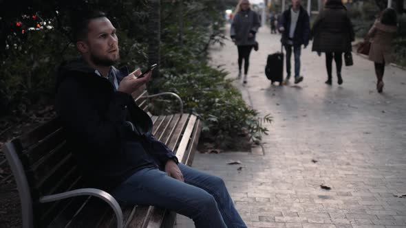 Casual Happy Man Using Smartphone Sitting on a Bench in Park Tourist Use Voice Recognition Ai Speech
