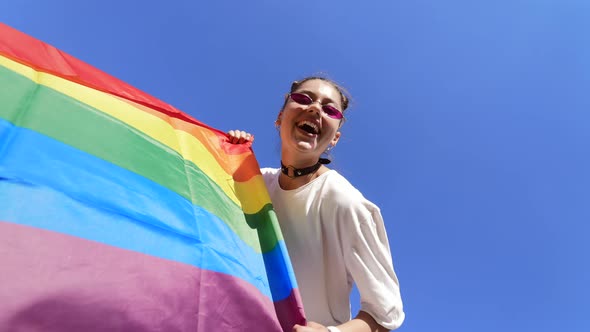 A Young Woman Develops a Rainbow Flag Against the Sky