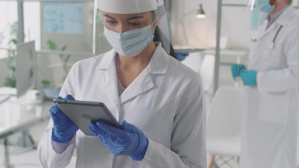 Female Doctor in Protective Uniform Using Tablet at Work