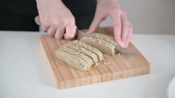 Young woman hands cut brown halva into slices on wooden cutting board with sharp steel knife