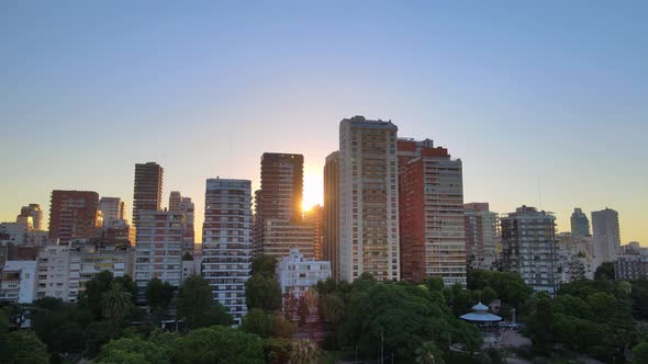 Aerial rising over park at sunset with sun setting behind buildings in Belgrano neighborhood, Buenos