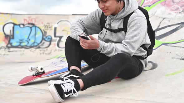 Young Latin Man Skateboarder, with Mobile Phone, Texting at Skate Park