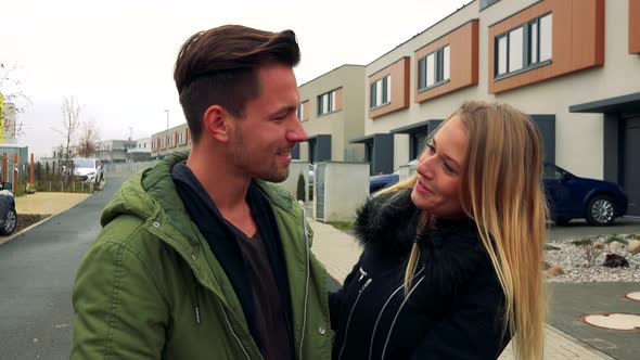 An Young Couple Greets Each Other with a Hug on a Road in a Neighborhood, Smiles and Laughs