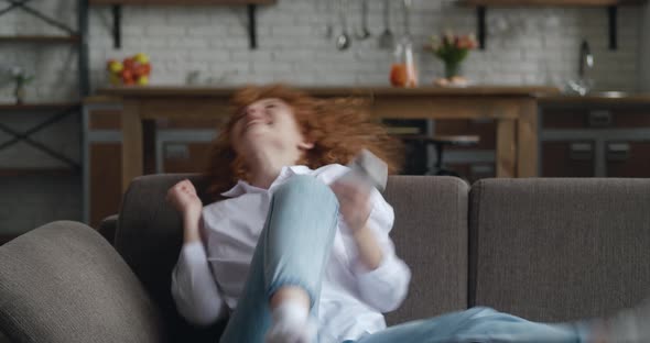 Overjoyed Young Redhead Woman Using Smart Phone Winning Gift or Prize in Social Media App Sit on