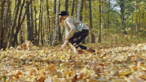 Laughing girl catching her dog in autumn forest