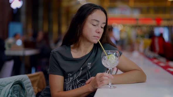 the Brunette is Sitting at the Counter and Thoughtfully Looks Into Glass Then Sips Through a Straw