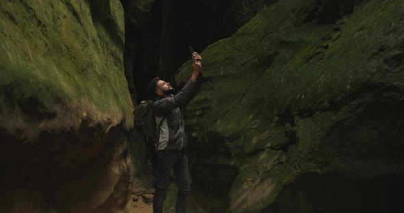 A Man is Standing in a Gorge and Shooting a Video on a Smartphone
