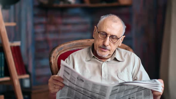 Gray Haired Aged Mature Man in Eyeglasses Reading Daily Press Printing Newspaper Vintage Armchair