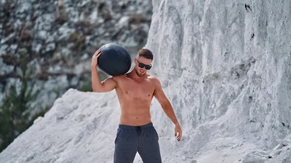 Bodybuilder training with a heavy ball in white mountains.