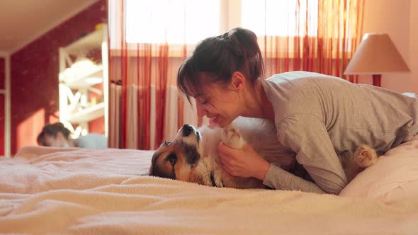 Smiling Woman with Dog in Bed at Home, Hugging Funny Yawning Dog Welsh Corgi