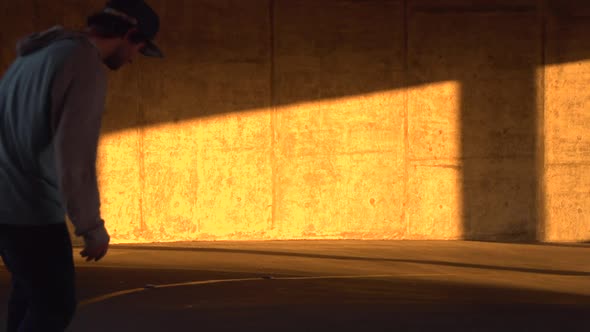 Silhouette of a young man skateboarding in a parking garage at sunset.