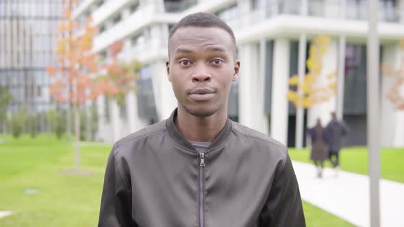 A Young Black Man Talks To the Camera - Office Buildings in the Blurry Background