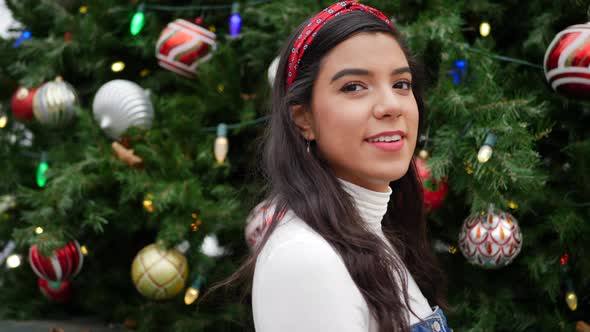 A cute young woman out Christmas shopping in the city with a tree decorated with ornaments and festi