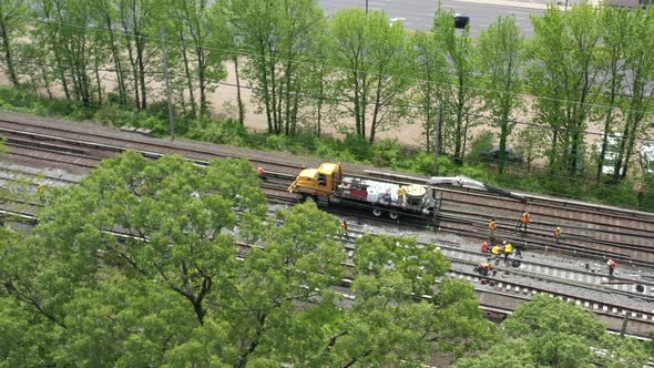 an aerial view over trees looking at men fixing train tracks on a sunny day. The camera focuses on a