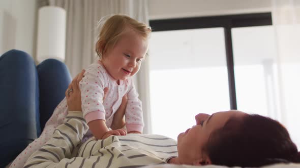 Caucasian mother smiling while playing with her baby on the bed at home