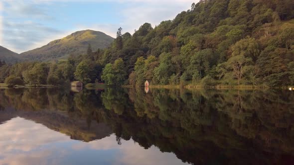 Mirror reflection of hills, woods and boathouses on Ullswater lake