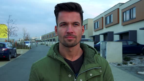 A Young, Handsome Man Points at the Came with a Finger and Nods, a Street in the Background