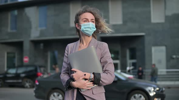 A young woman in a medical mask stands with documents in her hands