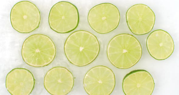 On a White Background, Sliced Pieces of Lime Are Sprinkled with Water. Juicy Fresh Lime in Slow