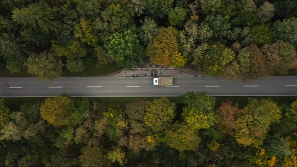 A fast driving lorry at a straight road in a autumn colored forest street, filmed from above by a dr