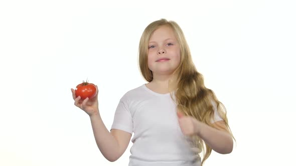 Kid Girl Looks at a Tomato, Admires It and Shows a Thumbs Up. White Background