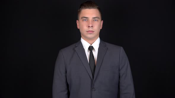 Young Businessman Shows a That Rocks Sign with Two Hands. Man in a Black Suit on a Black Background