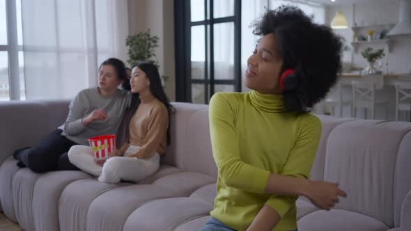 Happy Joyful African American Woman Enjoying Music in Headphones Dancing Sitting on Couch with