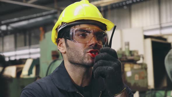 Factory Worker Talking on Portable Radio While Inspecting Machinery Parts