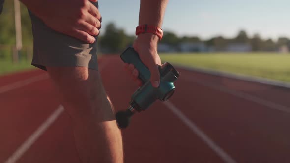 Athletic Male Massages Muscles with Hand Massage Gun Recovering From Stadium Running Workout